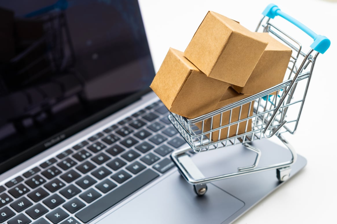 Playful shopping cart with cardboard boxes on a notebook. Consumer society trend