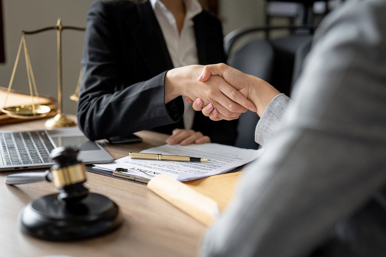 Gavel Justice hammer on wooden table with judge and client shaking hands after adviced in background at courtroom, lawyer service concept.